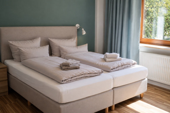Ankommen & wohlfühlen Helles Schlafzimmer mit Doppelbett, zwei Kissen, handtuch und einem Fenster.