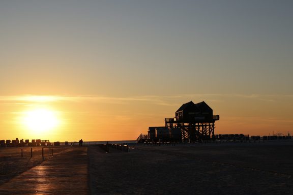 Pfahlbauten in St. Peter-Ording bei Sonnenuntergang Pfahlbau am Strand von St. Peter-Ording bei Sonnenuntergang mit Holzsteg und Nordsee-Kulisse.